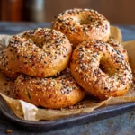 Shaped protein bagels topped with sesame and seasoning on a baking tray