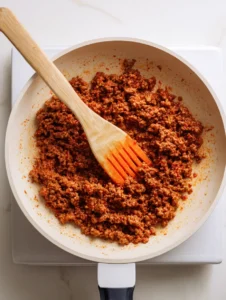 Cooking ground beef with taco seasoning in a white skillet